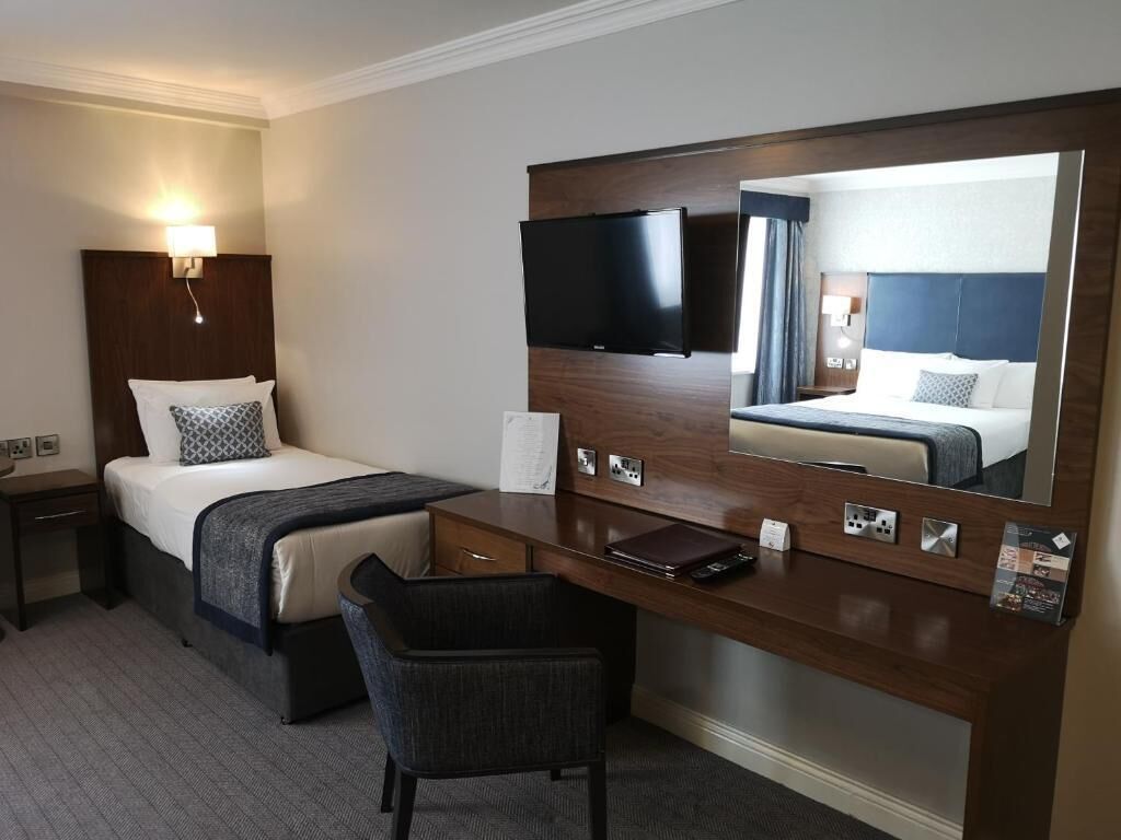 Une chambre d’hôtel équipée d’un lit, d’un bureau, d’une chaise, d’un grand miroir et d’un téléviseur à écran plat.