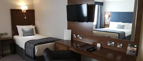 Une chambre d’hôtel équipée d’un lit, d’un bureau, d’une chaise, d’un grand miroir et d’un téléviseur à écran plat.