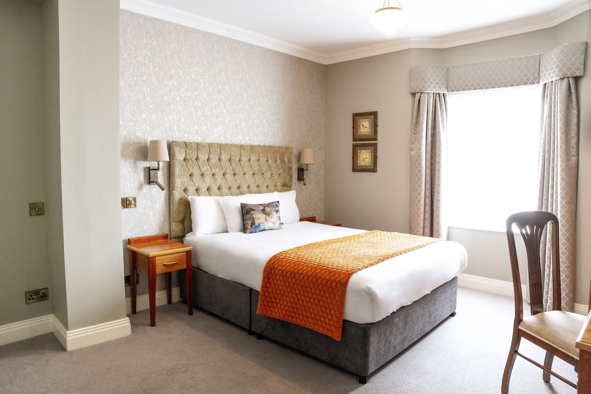 A hotel room with a large bed, a nightstand, a chair, and a window with curtains.
