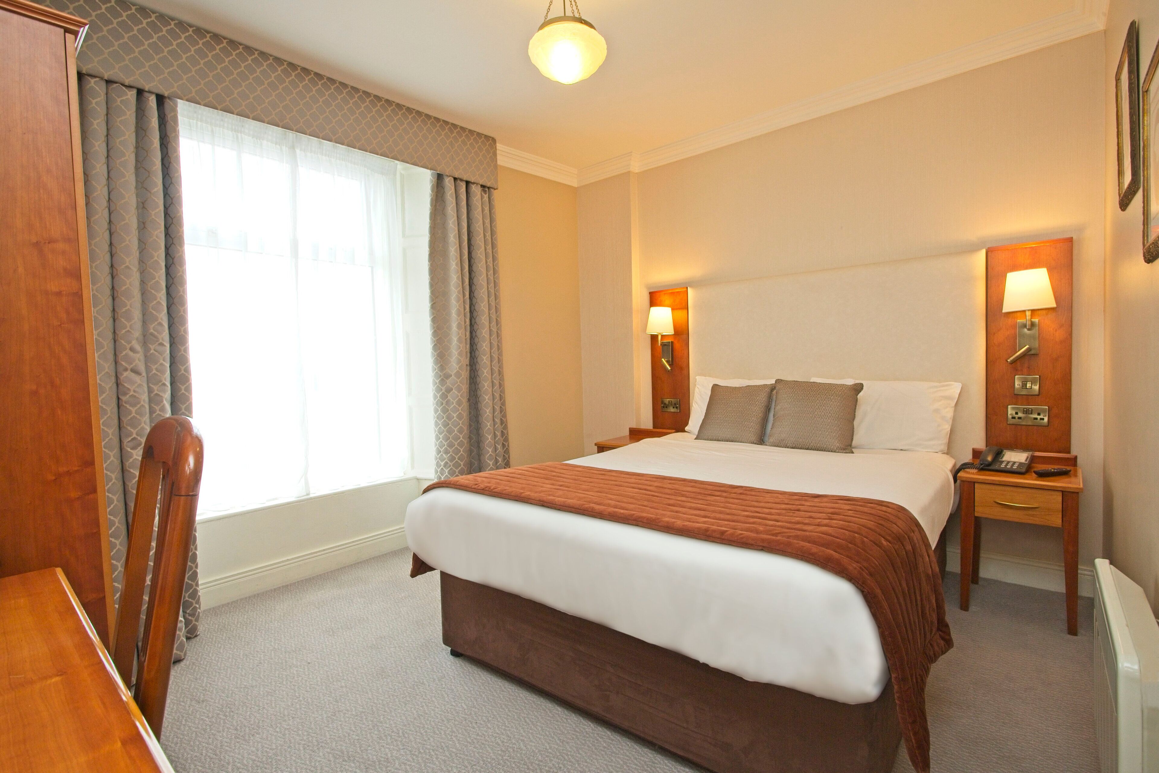 A hotel room with a large bed, two bedside tables with lamps, a wooden chair, and a desk.