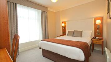 A hotel room with a large bed, two bedside tables with lamps, a wooden chair, and a desk.