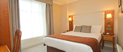 A hotel room with a large bed, two bedside tables with lamps, a wooden chair, and a desk.