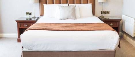 A neatly made bed with a brown headboard, white bedding, and two bedside tables with lamps.