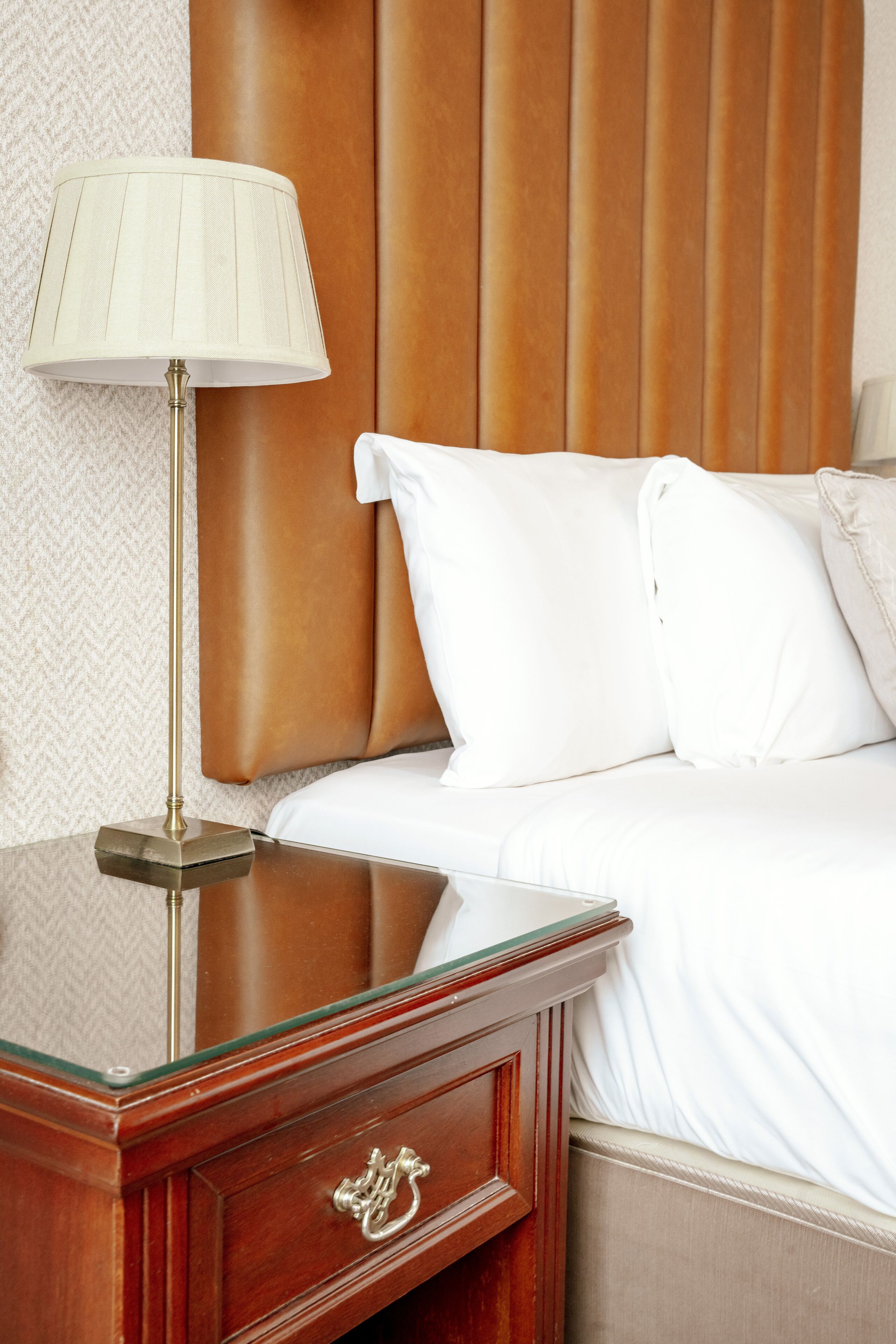 A neatly made bed with white linens, a wooden headboard, and a bedside table with a lamp.