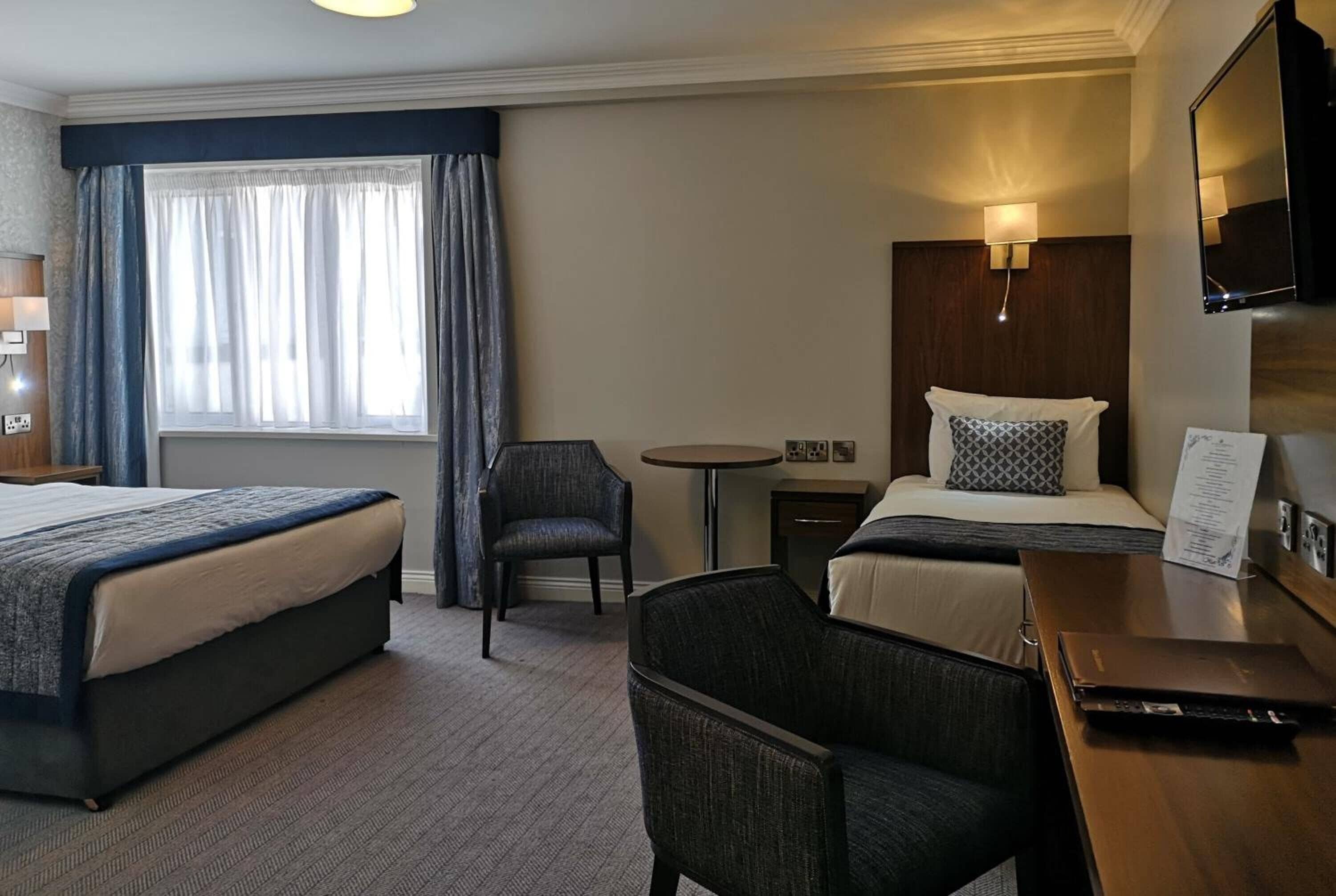 Une chambre d’hôtel avec deux lits, un bureau, une chaise, une petite table et un téléviseur.