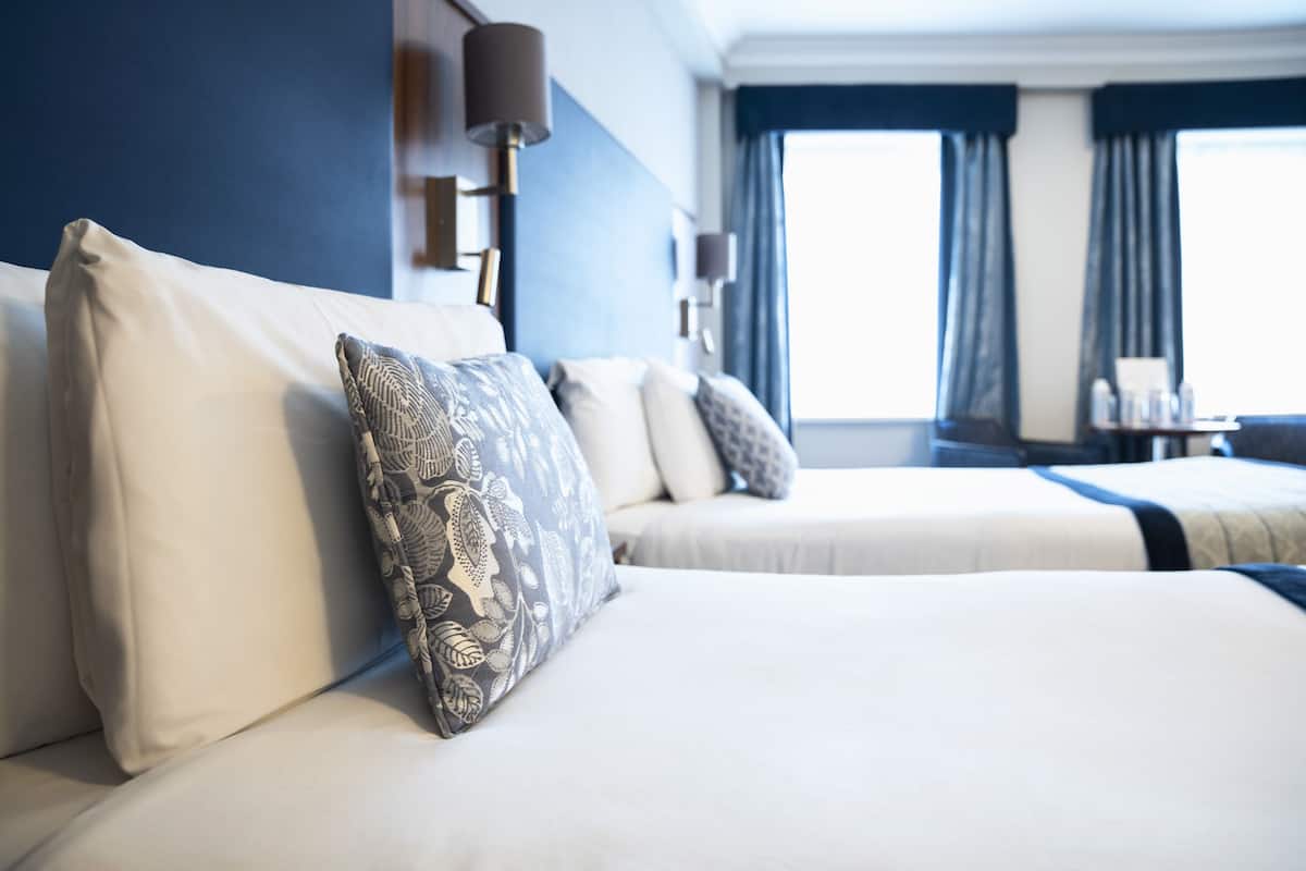A hotel room with two beds, a large window with curtains, and a desk with a lamp.
