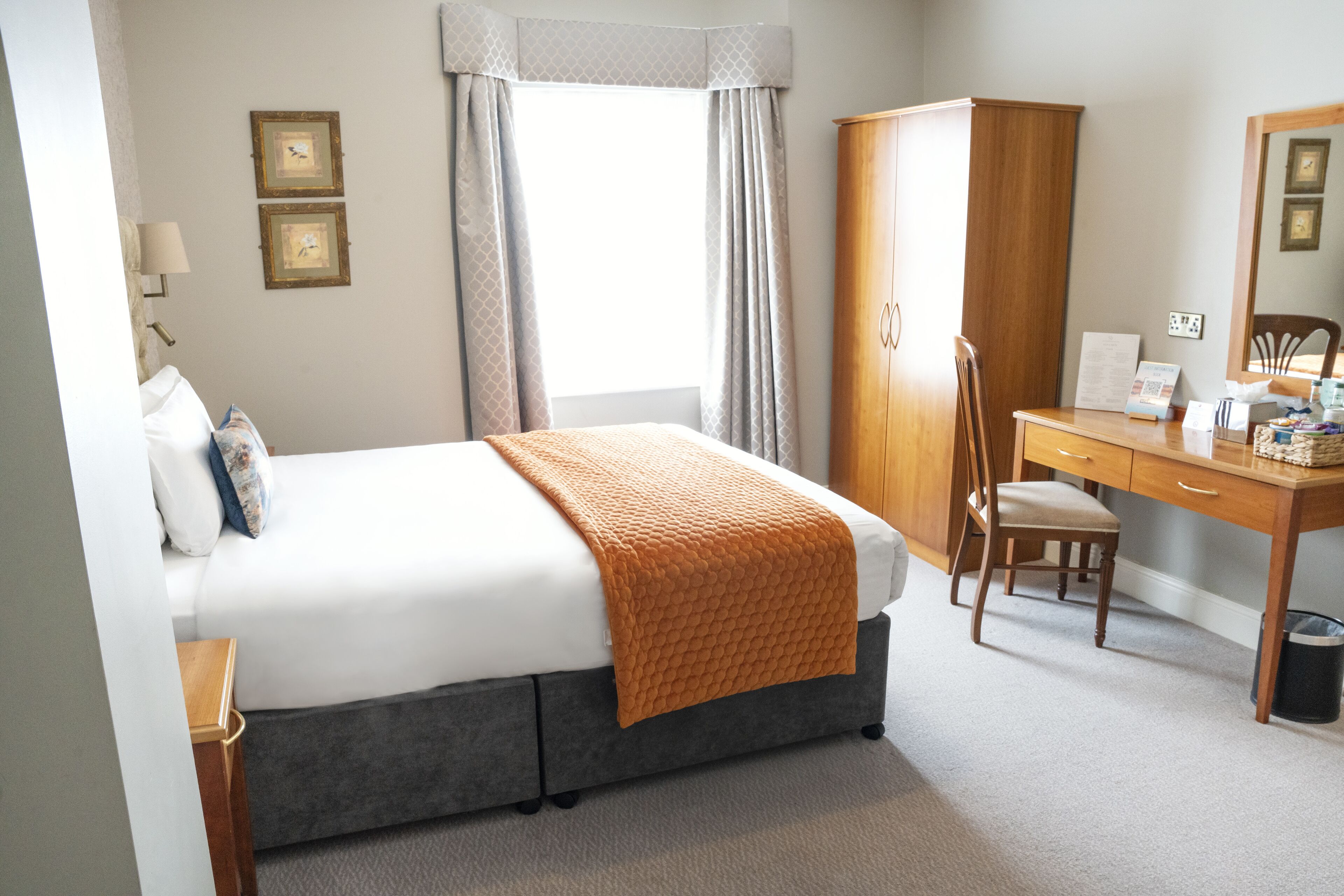 A neatly arranged hotel room with a bed, a desk, and a wardrobe.