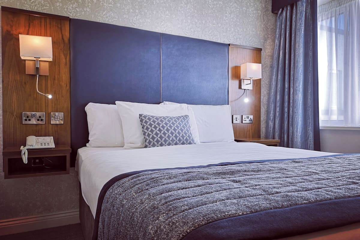 A hotel room with a bed, bedside lamps, a telephone, and a window with curtains.
