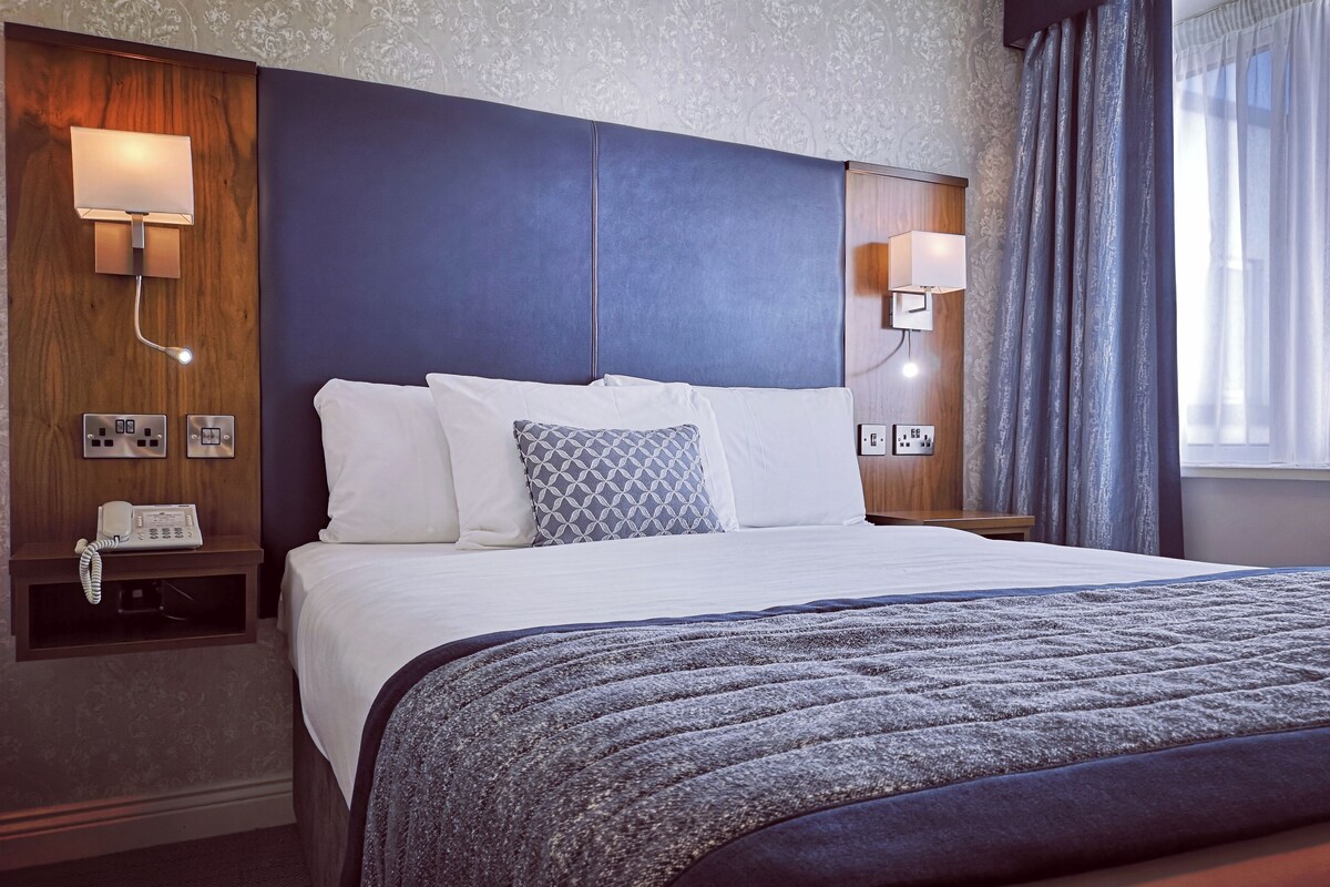 A hotel room with a bed, bedside lamps, a telephone, and a window with curtains.