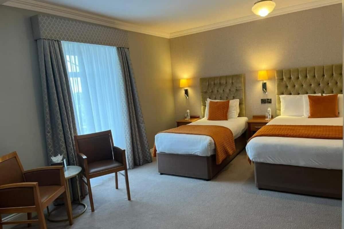 A hotel room with two beds, a chair, and a small table.