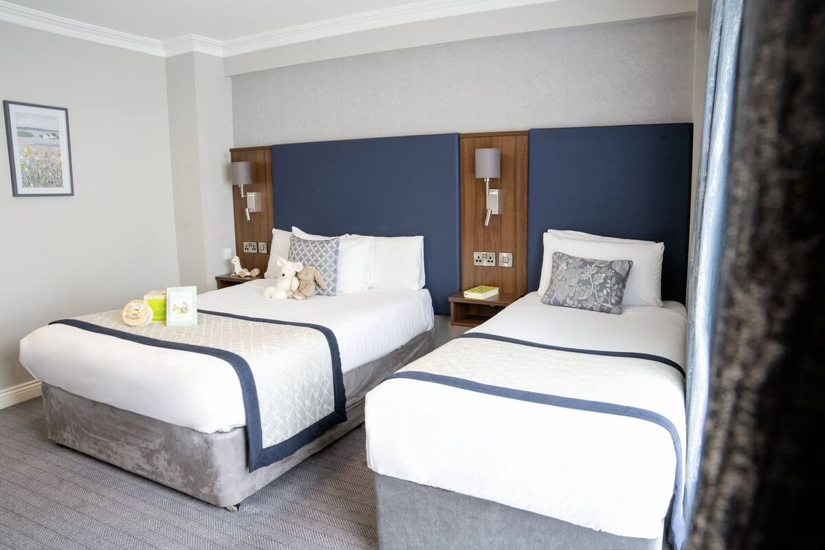 A hotel room with two beds, each with a headboard, bedside tables, lamps, and a framed picture on the wall.