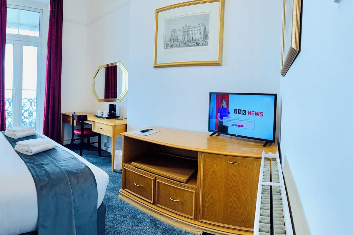 A hotel room with a bed, bedside table, lamp, desk, chair, television, and framed pictures on the wall.
