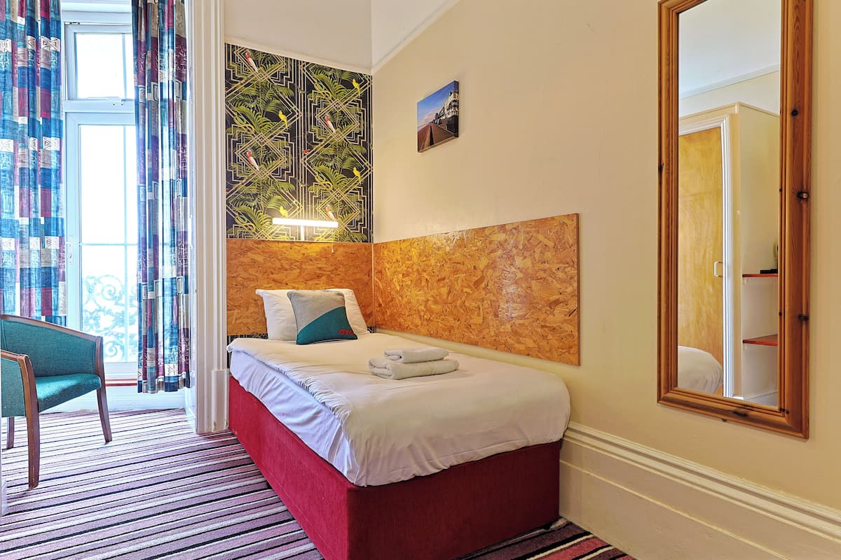 A hotel room with a bed, a chair, a large mirror, and a view of the outdoors.