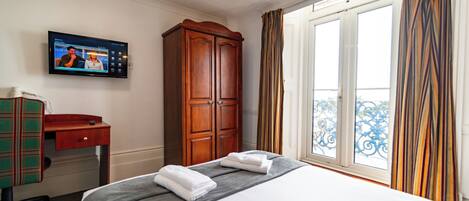 A hotel room with a bed, a desk, a wardrobe, a television, and a window with curtains.