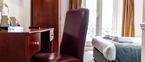 A hotel room with a desk, a chair, a bed, and a TV on the wall.