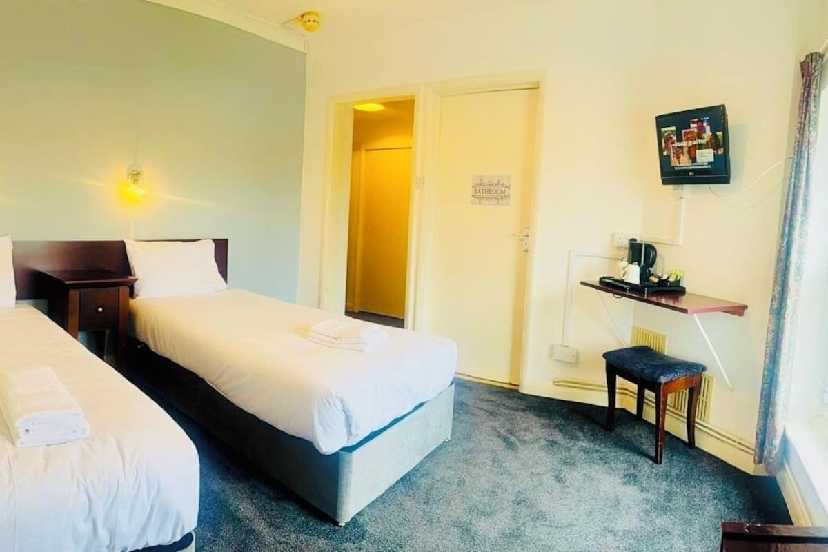 A hotel room with two beds, a small desk with a chair, a television, and a sign indicating a bathroom.