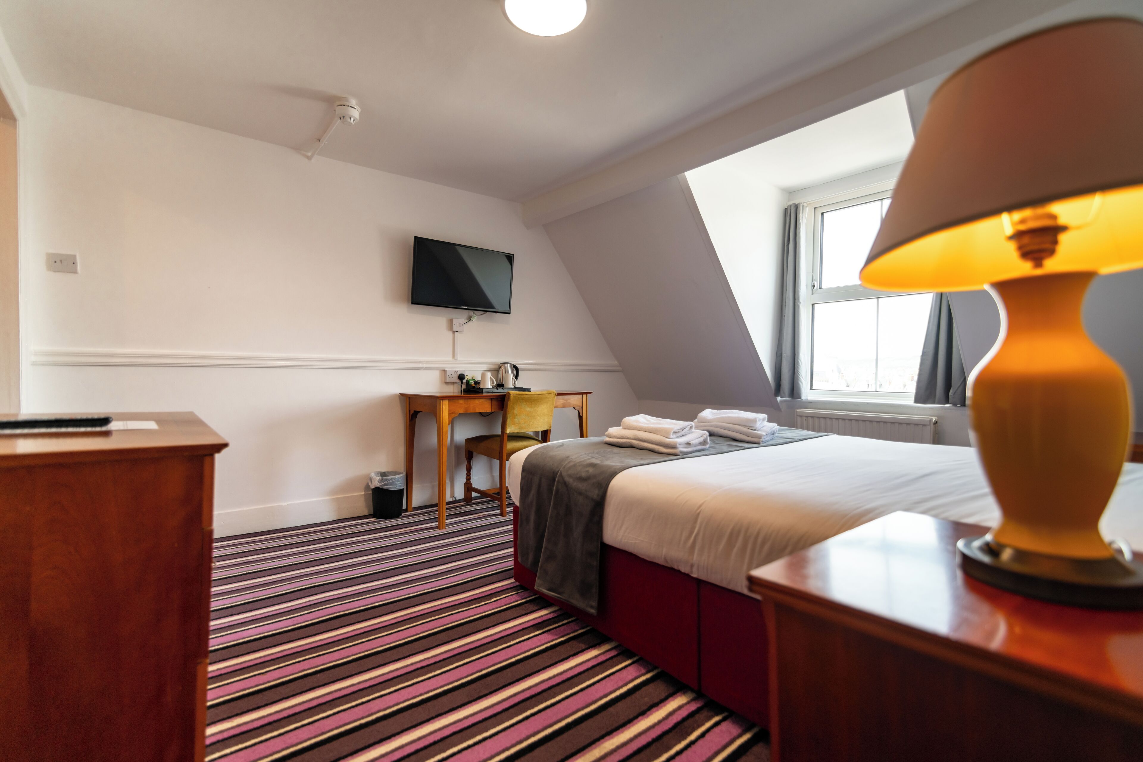 A hotel room with a bed, a desk, a chair, a television, and a window with curtains.