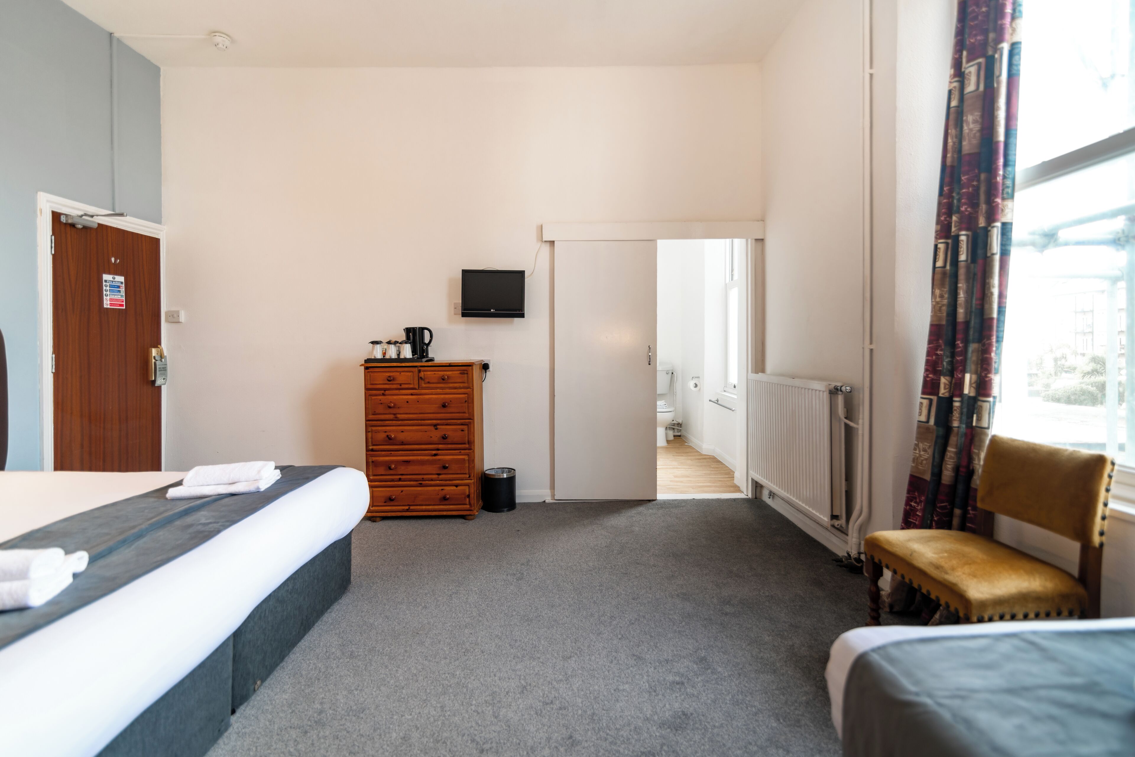 A hotel room with a bed, a dresser, a television, and a window with curtains.