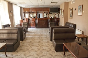 A hotel lobby with leather sofas, a wooden coffee table, and a bar area with a television.