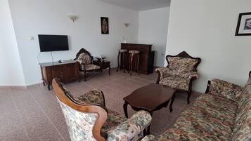 A living room with a sofa, armchairs, a coffee table, a TV, and a cabinet.