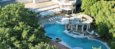 A multi-story building with a pool and outdoor seating area surrounded by trees.
