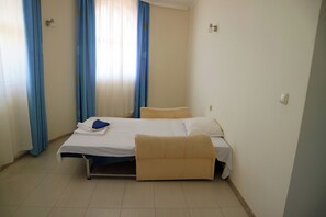A single-bed room with a pull-out sofa, a bedside table, and a window with blue curtains. - Park Hotel Bellevue (Golden Sands)