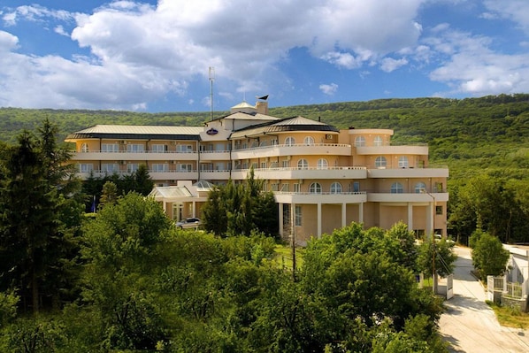 Ein mehrstöckiges Hotel mit Innenhof, umgeben von üppiger Vegetation und Hügeln im Hintergrund.