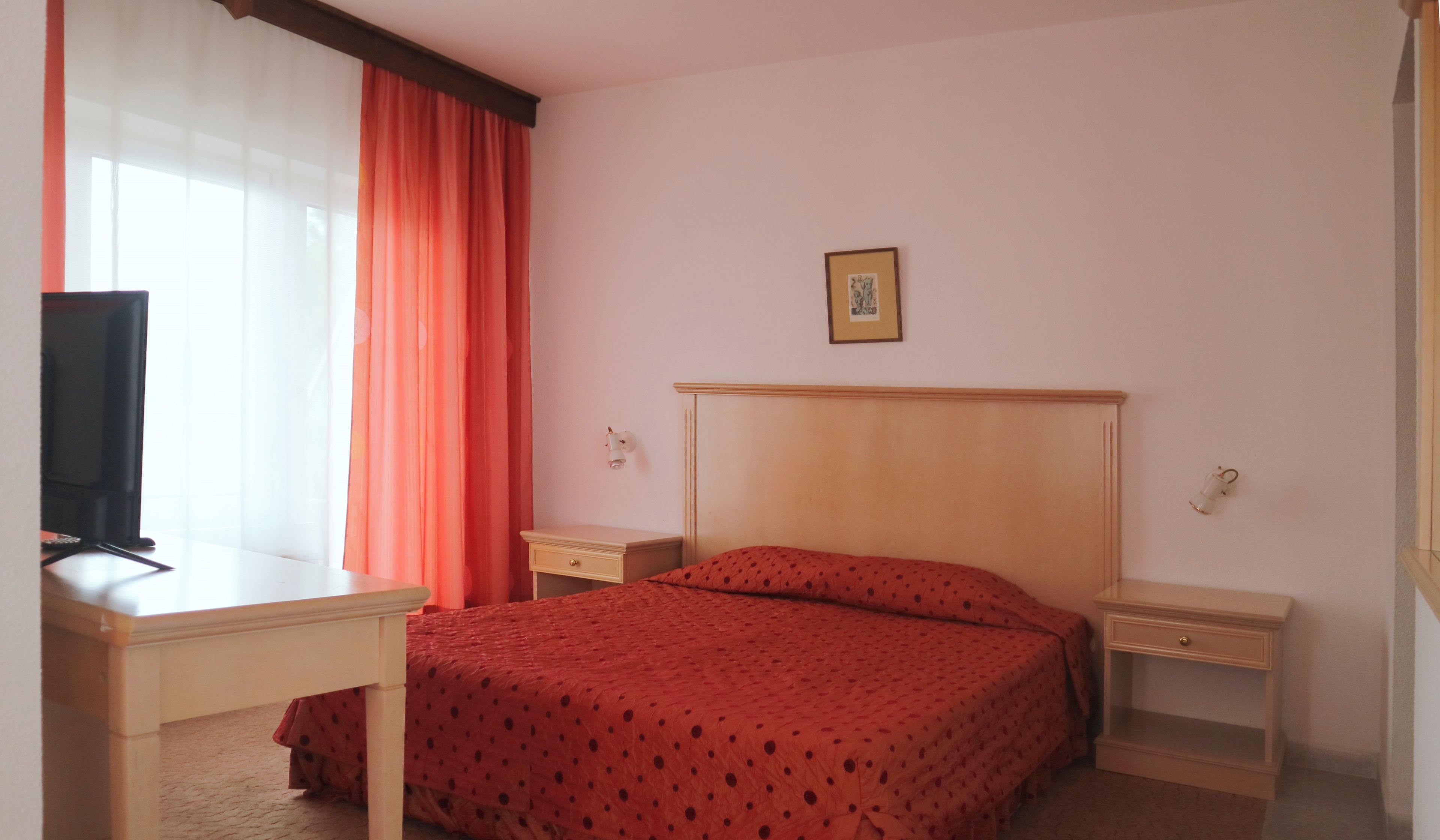 A hotel room with a bed, a desk, a chair, a television, and a nightstand.