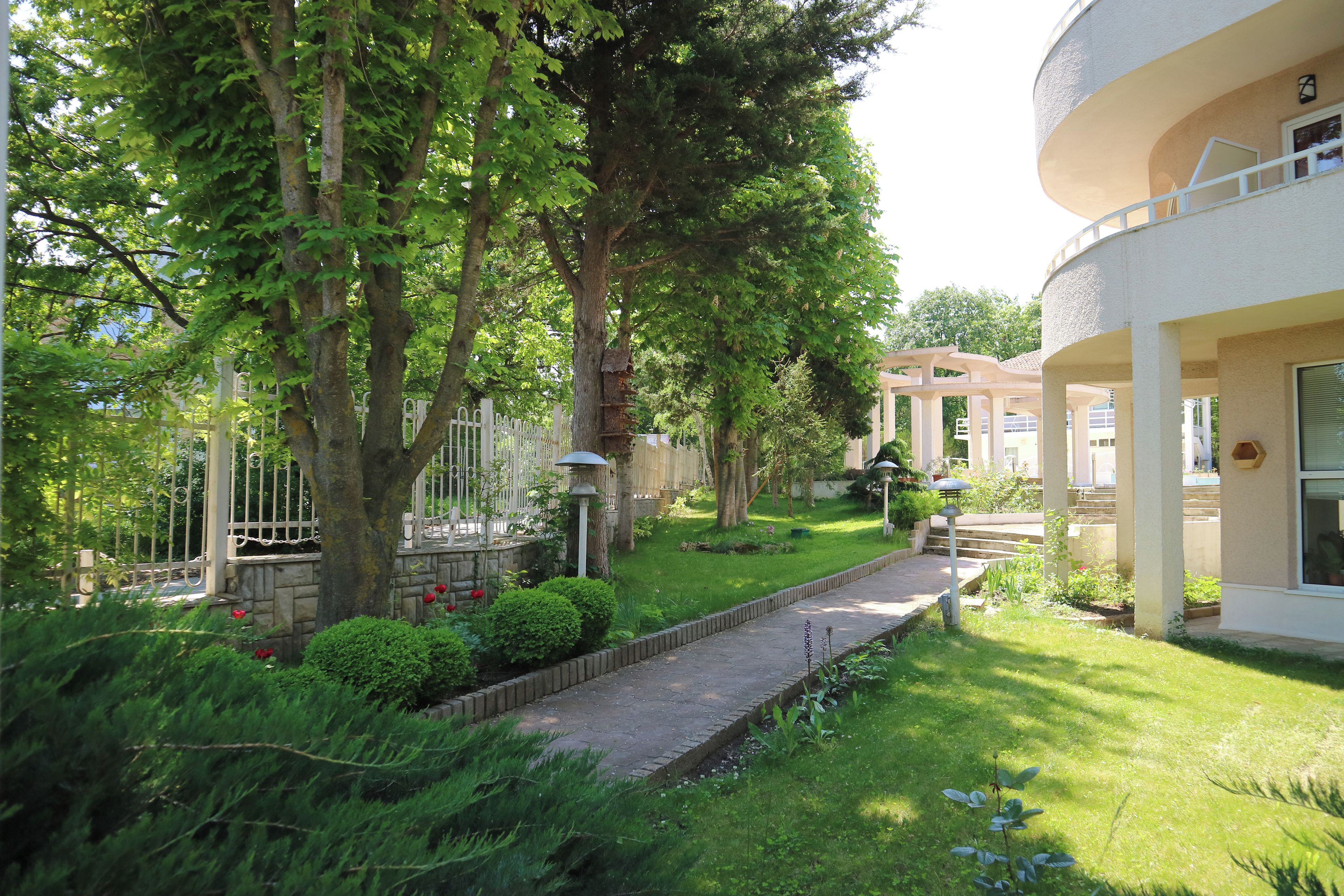 Ein Gartenweg führt zu einem Gebäude mit weißer Fassade und einem überdachten Bereich mit Säulen.