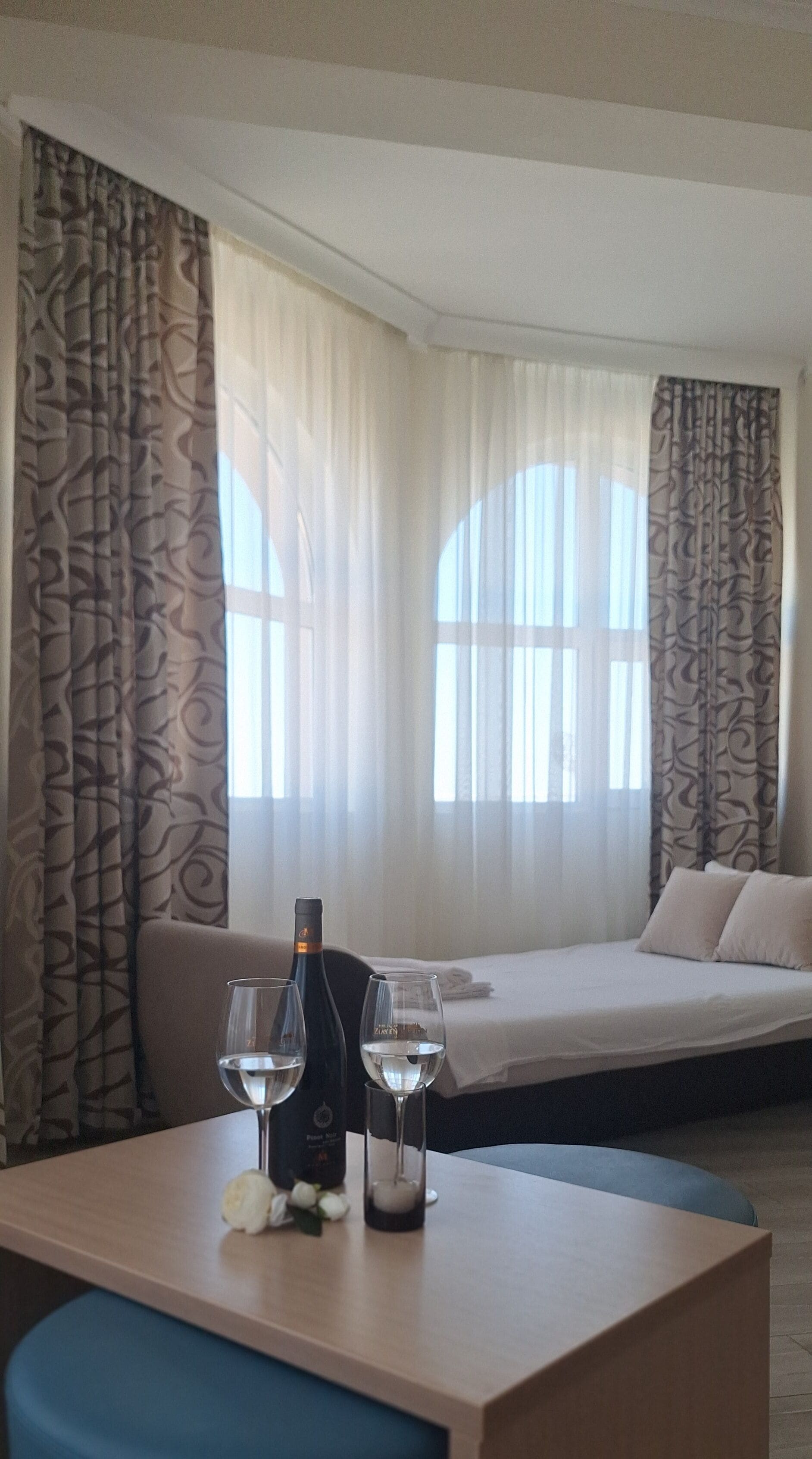 A hotel room with a bed, a table with two glasses of wine, and a bottle of wine.