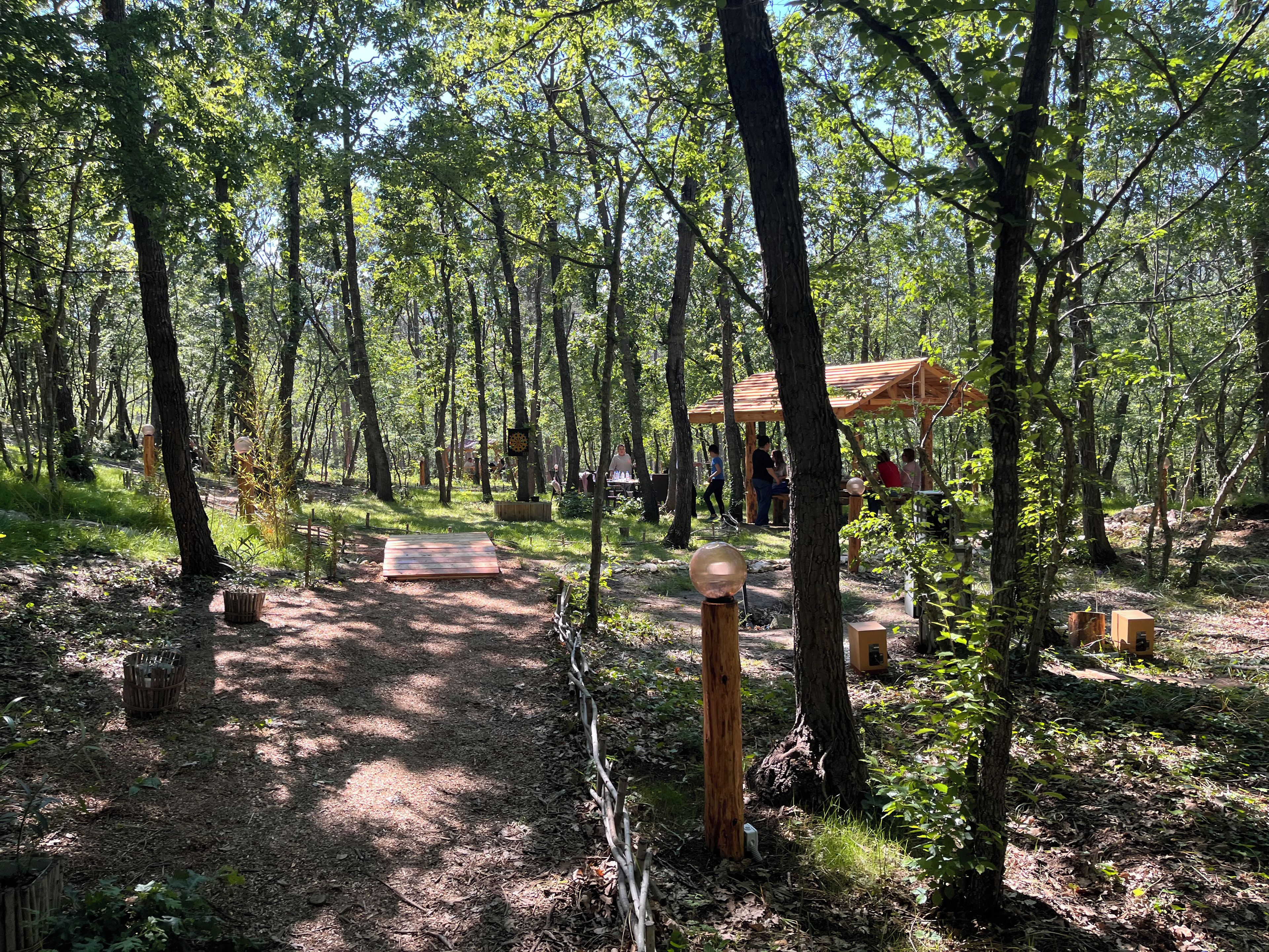 A forested area with a wooden structure, possibly a pavilion, and a dirt path leading through the trees.