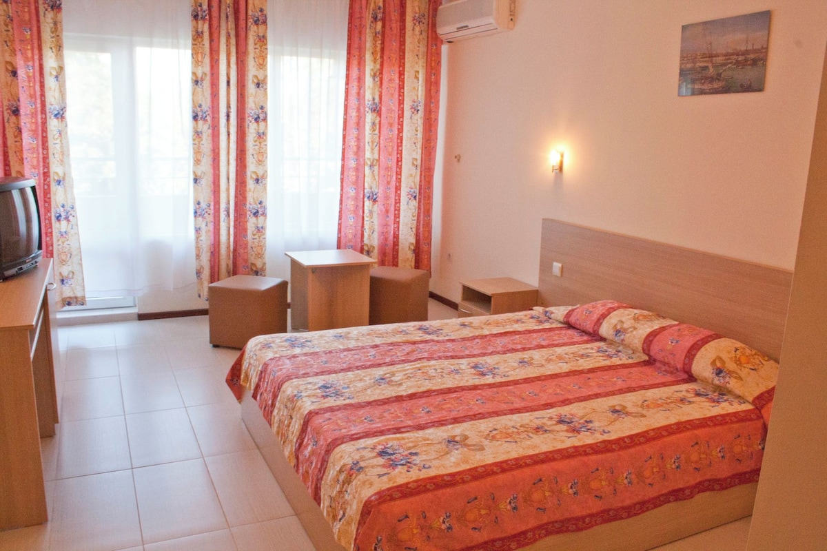 A hotel room with a bed, a desk, a chair, and a television.