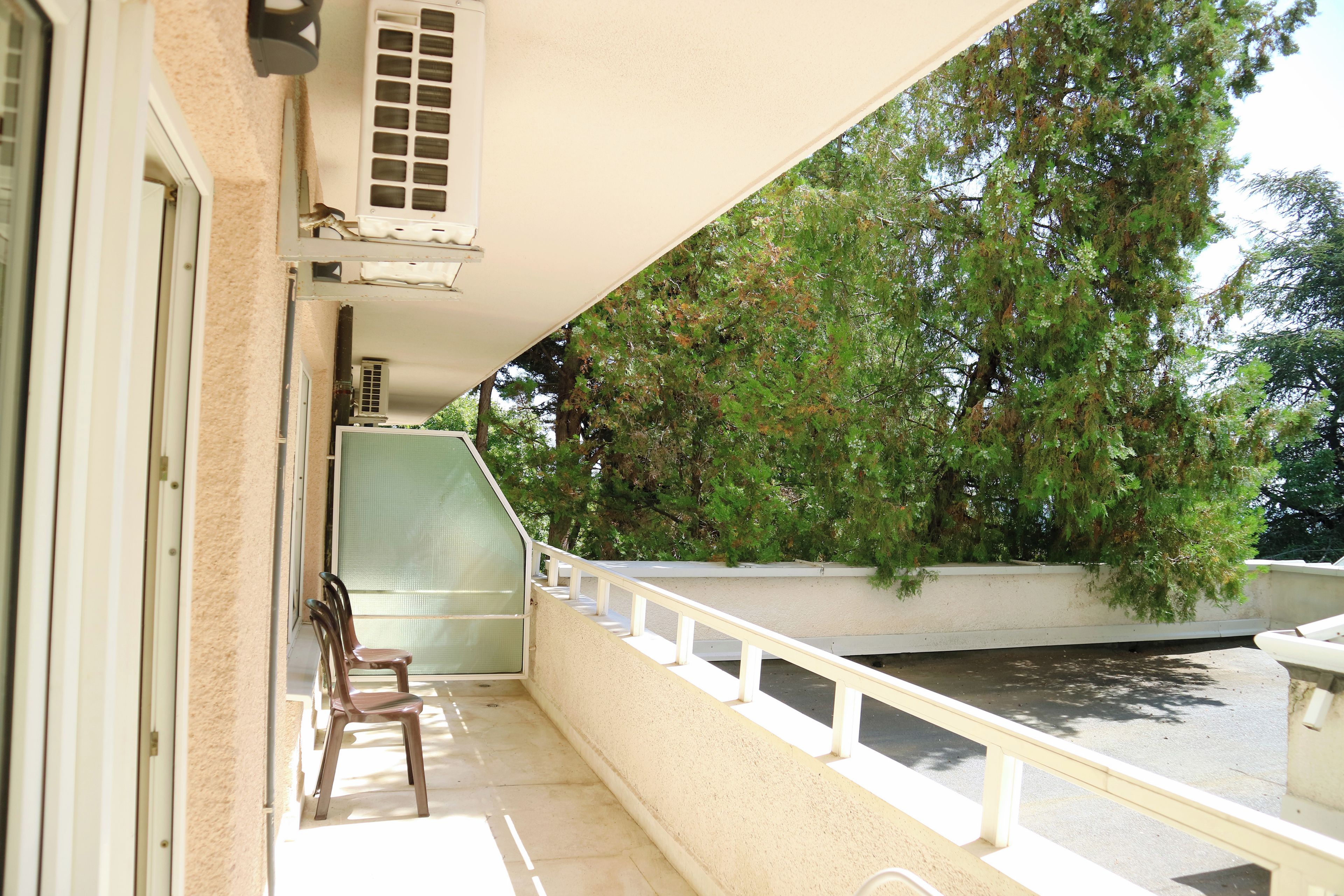 A balcony with a view of trees, a chair, and an air conditioning unit.