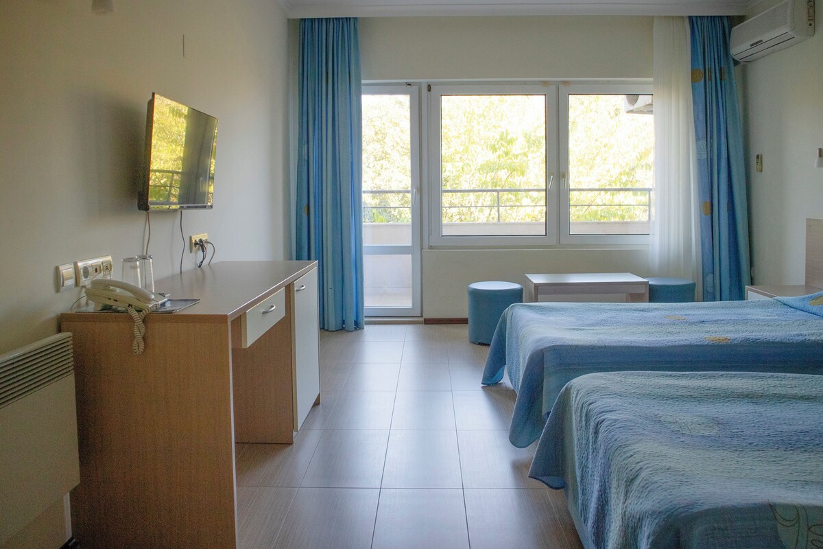 Habitación de hotel con escritorio, teléfono y cama con cubrecama azul.