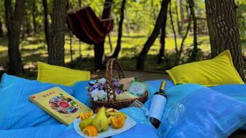 Montaje para un picnic sobre una manta azul en un bosque, con una cesta de mimbre, un menú, una botella de champán y un plato de fruta.