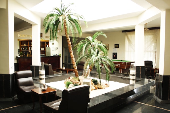 Eine Lobby mit Billardtisch, Ledersesseln, einer Rezeption und Palmen.