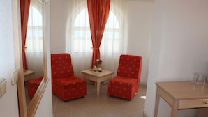 Una habitación con dos sillones tapizados de rojo, una mesita con un florero y un escritorio de madera con vasos.