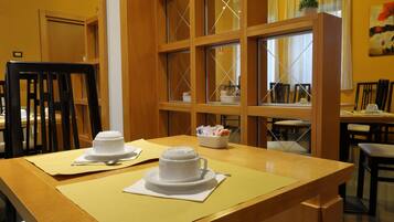 A dining area with a wooden table, two white plates with a white bowl, and a window with a view of another room.