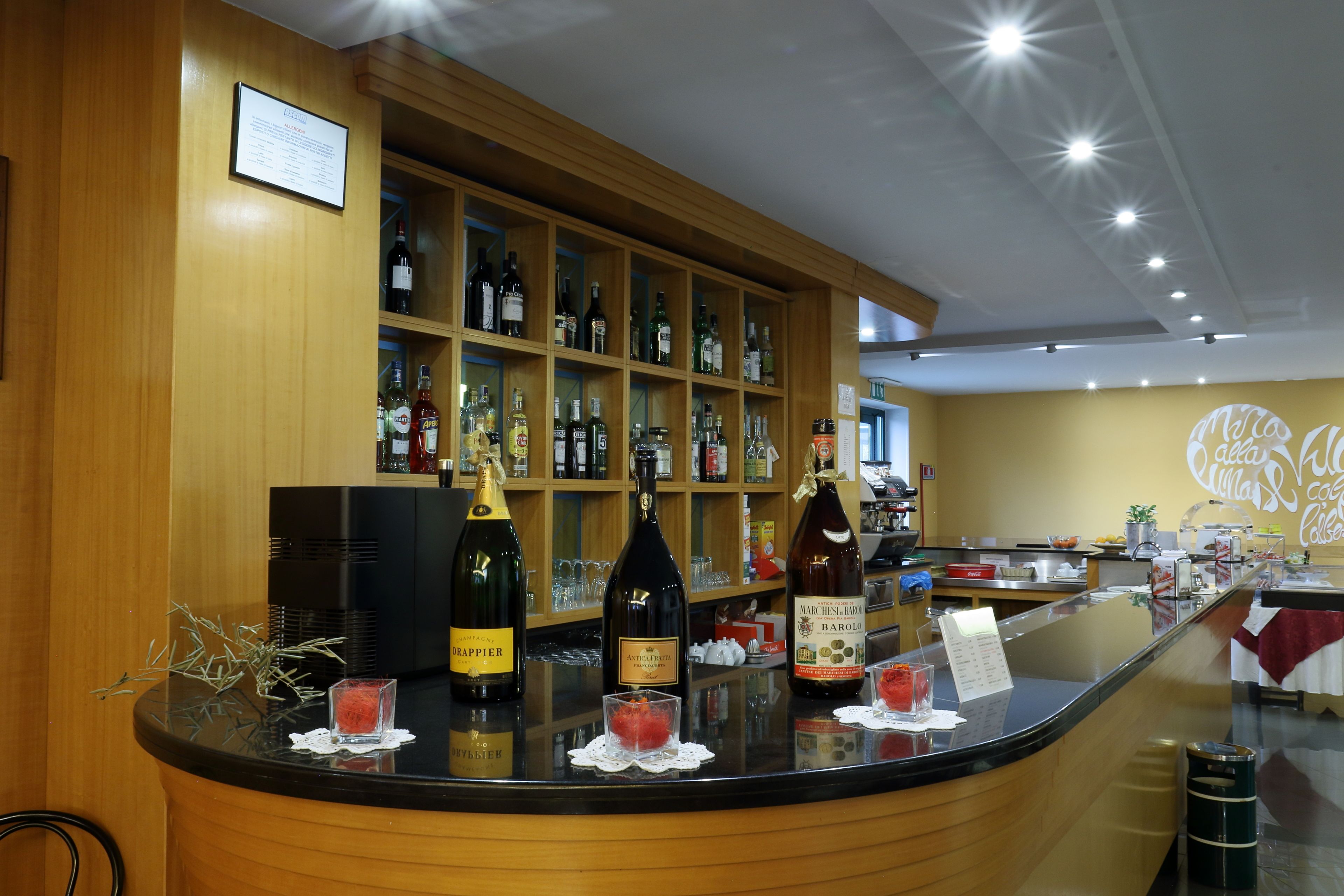 A bar area with shelves of liquor bottles, a counter with glasses and a menu, and a wall with a logo.