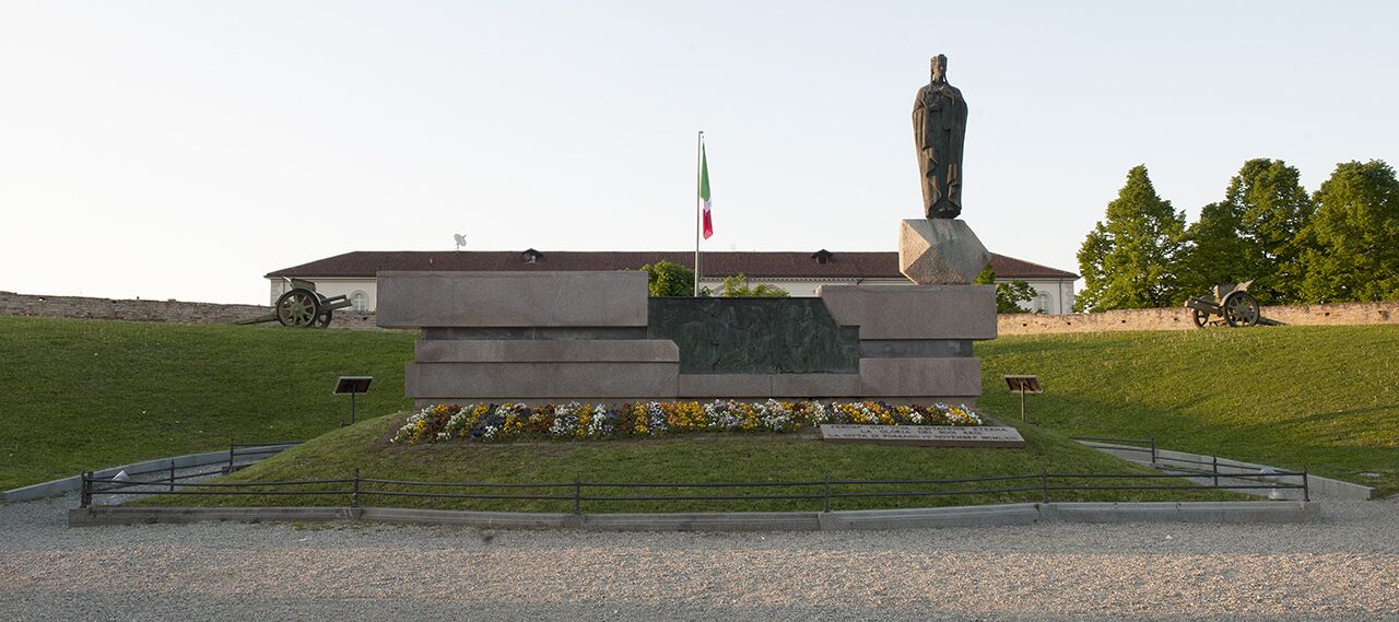 A memorial monument with a statue, surrounded by a landscaped area with flowers and a flag.