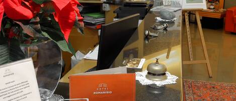 A reception desk with a sign for Hotel Romanianio, a potted plant, and a menu.