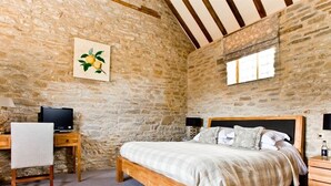A bedroom with a stone wall, a bed with a wooden frame, a desk with a computer, and a window. - Old Downton Lodge (Ludlow)