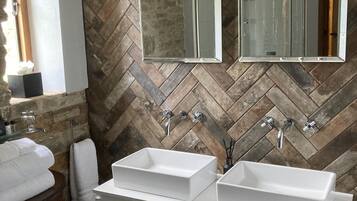 A bathroom with two white sinks, a wooden vanity, and a herringbone-patterned tiled wall.