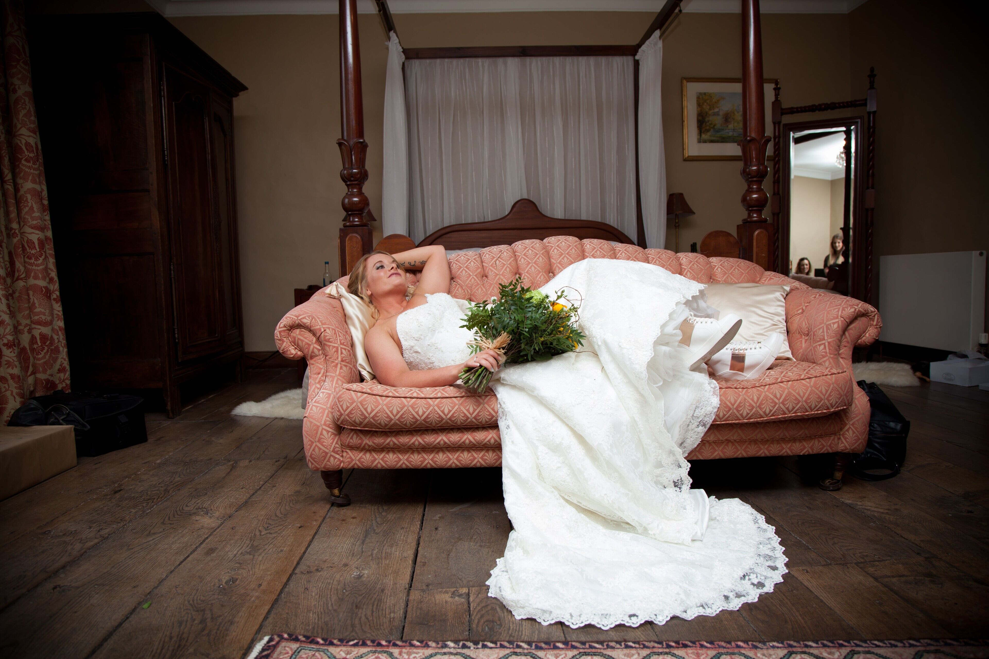 A bedroom with a four-poster bed, a wooden wardrobe, and a patterned sofa.