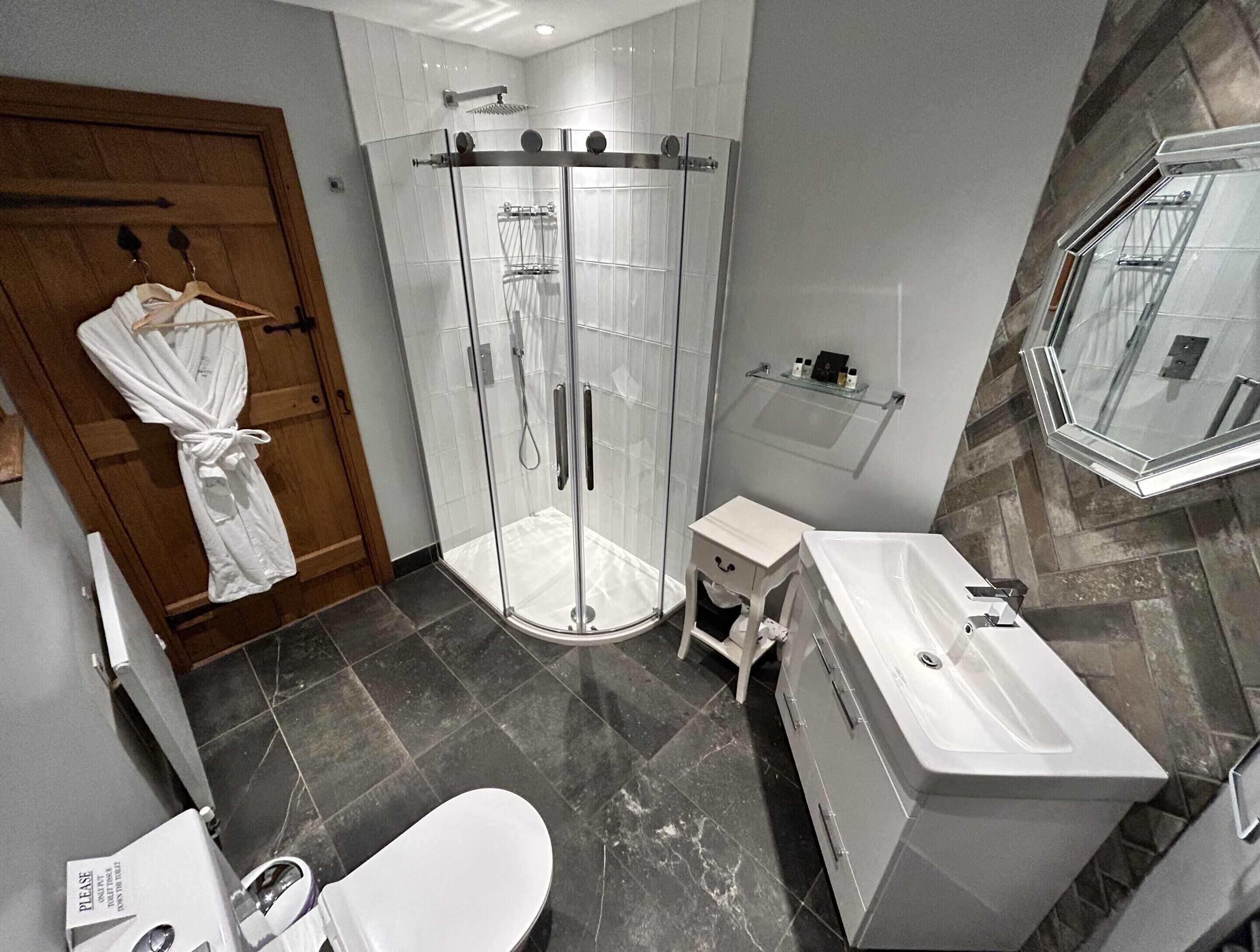 A modern bathroom with a glass-enclosed shower, a white sink, and a wooden door.