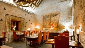 A rustic dining area with stone walls, wooden beams, and a large mural. Tables are set with red chairs and candles. - Old Downton Lodge (Ludlow)