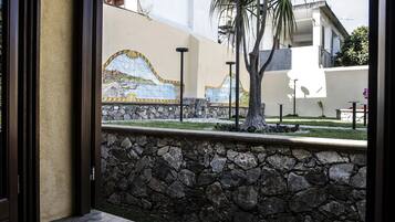 A stone wall with a mosaic mural, a palm tree, and a modern building in the background.