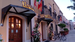 Entrada de hotel con una puerta doble de madera, un cartel sobre la puerta y plantas en macetas.