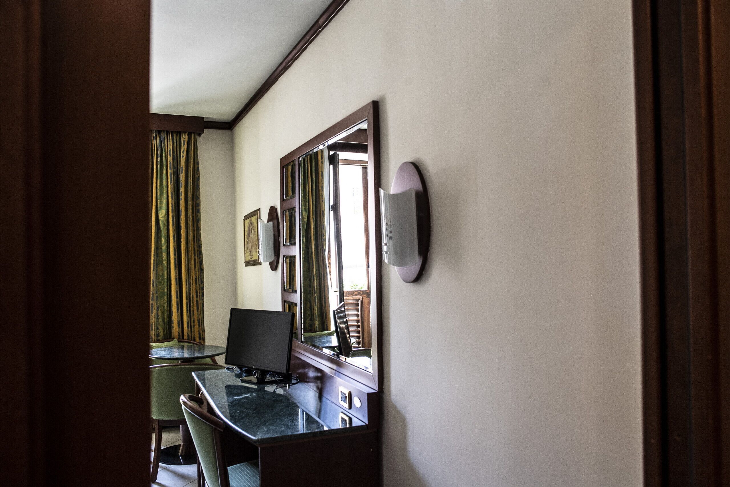 A hotel room with a desk, chair, and a large mirror.