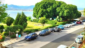 Un aparcamiento con coches, un parque grande y verde, y vistas al mar.